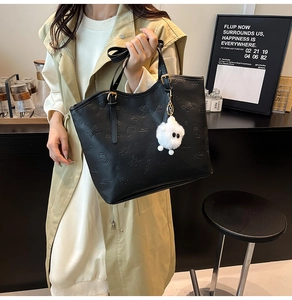 Détail du cabas en cuir noir avec motifs gaufrés et breloque en peluche blanche moelleuse