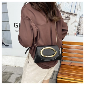 Close-up of black leather shoulder bag with gold C-buckle and metal chain strap