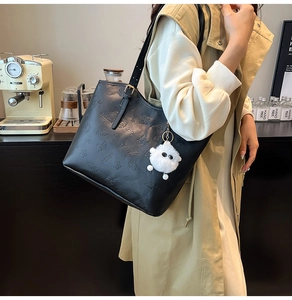 Close-up of black leather tote bag with embossed butterfly patterns and white plush charm
