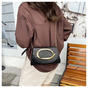 Detail of a black crossbody bag with gold C-buckle and chain strap on a model