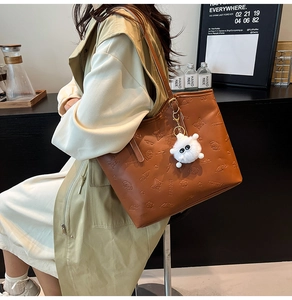 Détail d'un grand cabas marron gaufré avec motifs cartoon et breloque peluche monstre