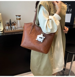 Side view of a brown embossed tote bag with a white plush monster charm on a model