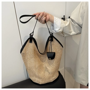 Detail of woven straw tote bag with black leather handles and mesh texture