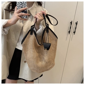 Detail view of woven straw tote bag with black leather trim and decorative pendant