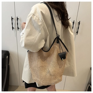 Large straw tote bag with black leather straps and bell charm shown on model's shoulder