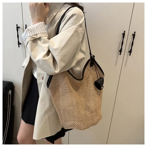 Detail of woven straw tote bag with black shoulder straps and a leather ball charm accessory