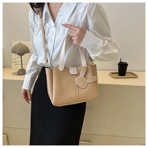 Close-up of khaki leather bucket bag with white handle and cute bunny charm decoration