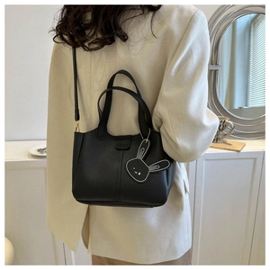 Detail of black leather bucket bag featuring a fashion rabbit charm and shoulder strap