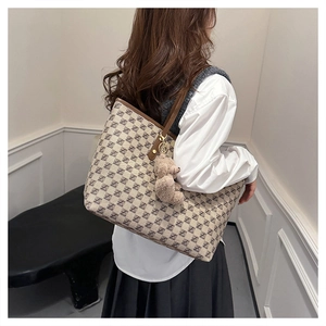 Detail of canvas tote bag with letter pattern, leather trim and bear pendant on model