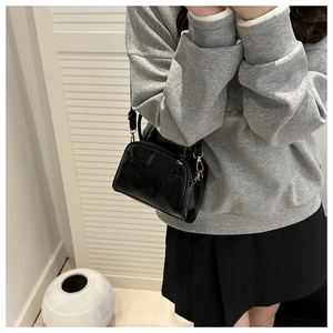 Détail d'un sac à main en cuir verni noir avec ferrures dorées porté par un modèle