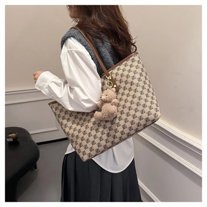 Detail view of large tote bag with monogram pattern and plush bear charm on model