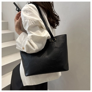 Detail of minimalist black PU leather tote bag with subtle texture and gold hardware