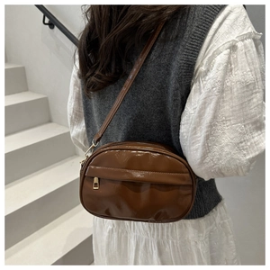 Close-up of brown glossy crossbody bag with metallic zipper on modern staircase