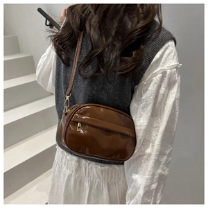 Detail of brown glossy crossbody bag with front zipper pocket and adjustable strap
