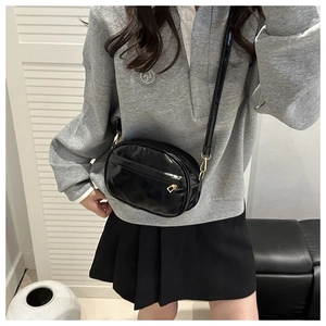 Detail of glossy black patent leather crossbody bag with golden metal hardware