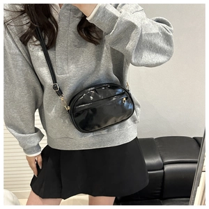 Detail of glossy black patent leather crossbody bag with adjustable strap worn by model