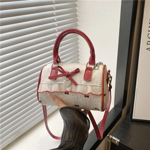 Chic cream underarm bag with red bow print and ruffle details, shown held by hand