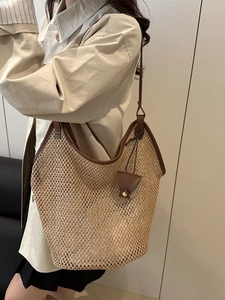 Large woven straw tote bag with brown trim shown on shoulder for beach and summer travel