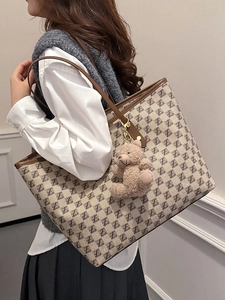 Beige tote bag with letter print and plush bear charm shown on a model for daily commute