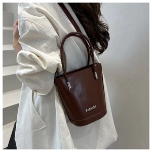 Detail of a dark brown leather bucket bag with white Fashion print and silver metal hardware
