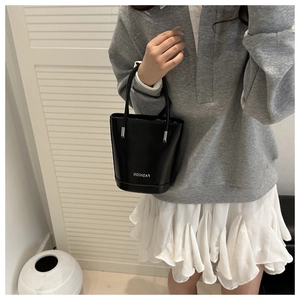 Detail of a black leather bucket bag with fashion lettering and silver metal hardware