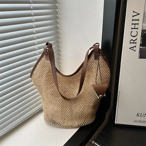 Summer woven tote bag with brown leather trim and triangle charm on a white windowsill