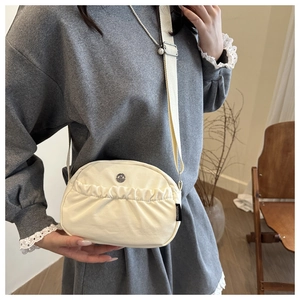 Macro detail of cream canvas crossbody bag showing side brand tag and ruffles