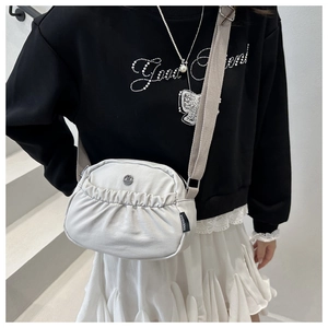 Close-up of a light grey pleated nylon crossbody bag with adjustable strap on a model
