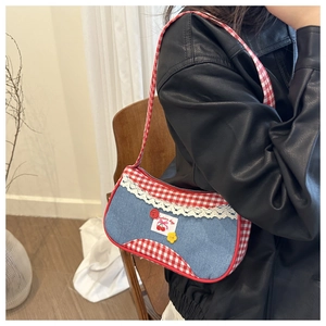 Close-up of denim shoulder bag featuring red plaid straps and delicate lace trim details