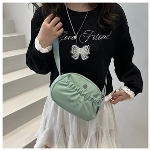 Detail of mint green nylon crossbody bag with pleated texture and round metal logo plate