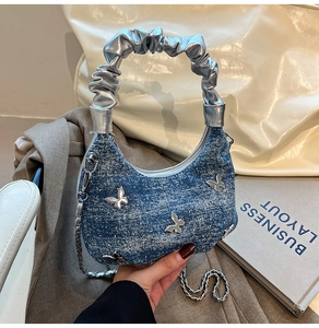 Detail of blue denim handbag featuring silver butterfly charms and pleated metallic handle