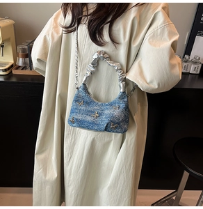 Détail du sac seau en denim bleu avec papillons argentés et poignée métallique plissée
