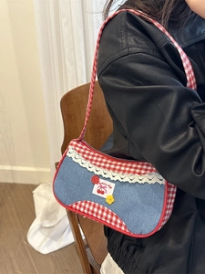 Sac bandoulière en denim avec bordure vichy rouge et écusson cerise porté par un mannequin