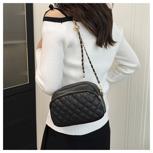 Detail of black quilted leather crossbody bag with dual zippers and gold chain strap