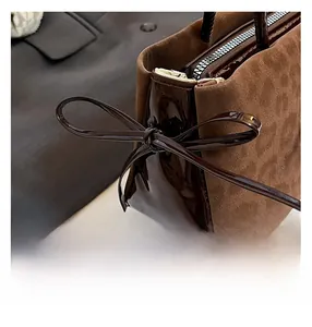 Close-up of brown patchwork handbag featuring textured suede and a glossy leather bow detail
