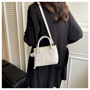 Detail of off-white lychee texture handbag with lace bow and pearl charm accents