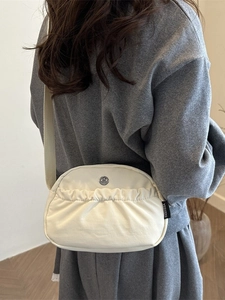 Chic beige canvas crossbody bag with pleated detail and adjustable shoulder strap