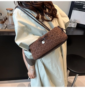 Detailed view of brown leopard print baguette bag with bow and heart charm on a model