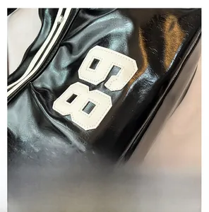 Close-up of black patent leather bag featuring a large white knitted 85 number patch
