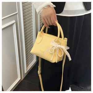 Detail of yellow lychee leather handbag with pearl bow pendant and crossbody strap