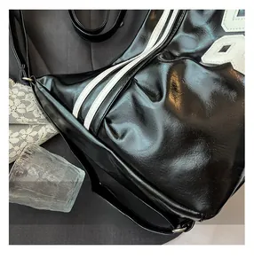 Macro detail of glossy black leather bag with white side stripes and stitched letter R