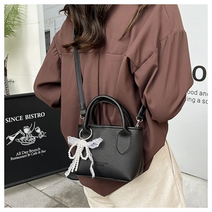 Mini black bucket bag with lychee texture, pearl lace bow charm, and crossbody strap
