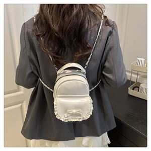 Détail du mini sac à dos blanc avec bordure en dentelle, nœud et bandoulière chaîne
