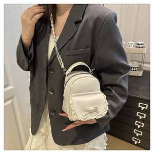 Détail du mini sac à dos blanc avec dentelle, nœud et bandoulière chaîne argentée