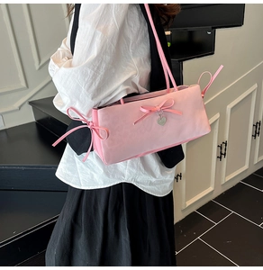 Detail of pink shoulder bag featuring a decorative bow and silver heart charm pendant