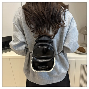 Detail of mini black backpack with white lace trim, bow, and silver chain strap