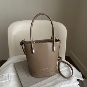 Minimalist brown PU leather bucket bag with top handle and shoulder strap on white chair