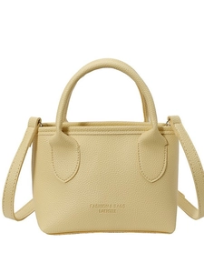 Pale yellow leather bucket bag with top handle and crossbody strap on a white background