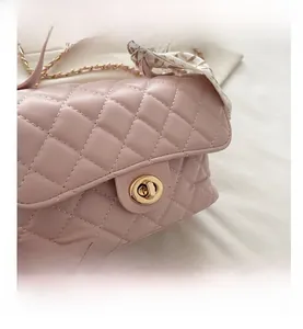 Close-up of pink quilted box bag featuring a gold turn-lock and silk scarf handle detail