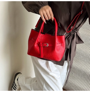 Sac à main tressé rouge avec boucle métallique porté par un mannequin en escalier
